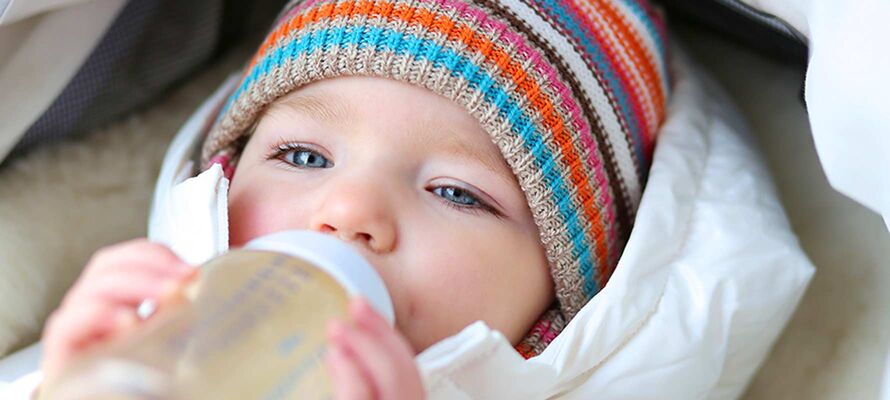 Baby in Kinderwagen liegend trinkt aus einem Fläschchen