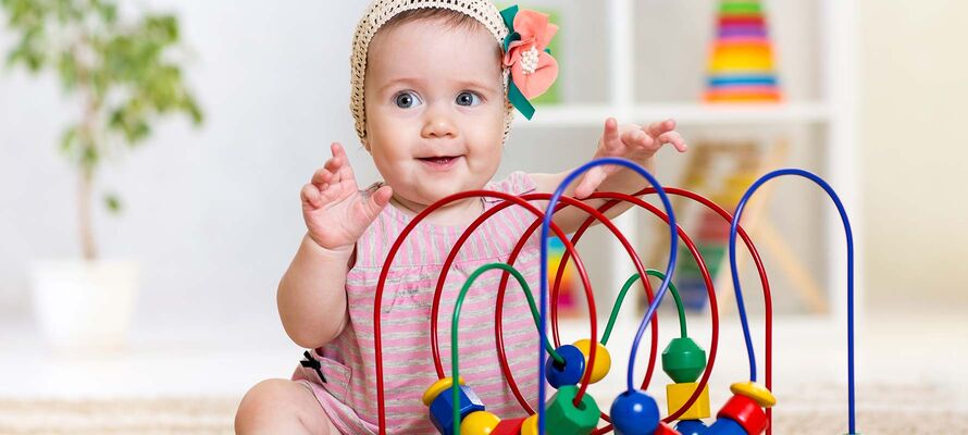 sitzendes Baby vor Spielzeug mit bunten Holzklötzen auf Spirale